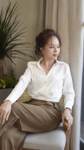 Phụ nữ thanh lịch mặc áo sơ mi trắng và quần nâu tối giản, phong thái chuyên nghiệp và trưởng thành