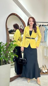 Phụ nữ phối đồ thanh lịch với áo vàng và chân váy dài tối giản trước gương tại cửa hàng Thắm Đặng